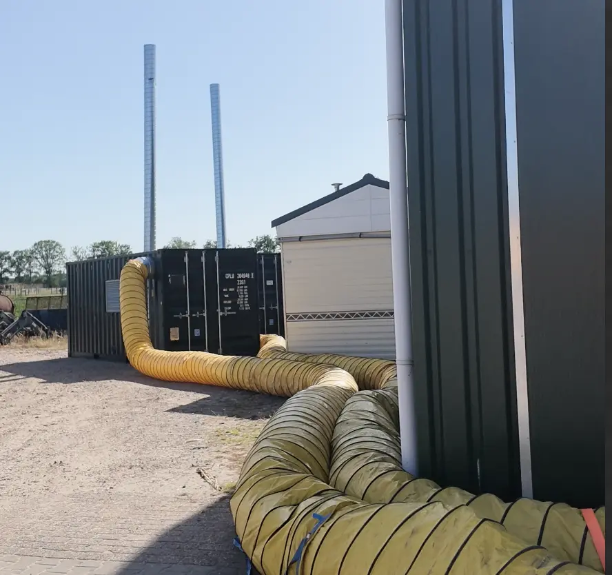 LANOX Warmluft-Ofen im Container mit gelben Warmluftschläuchen zu einem Gewächshaus